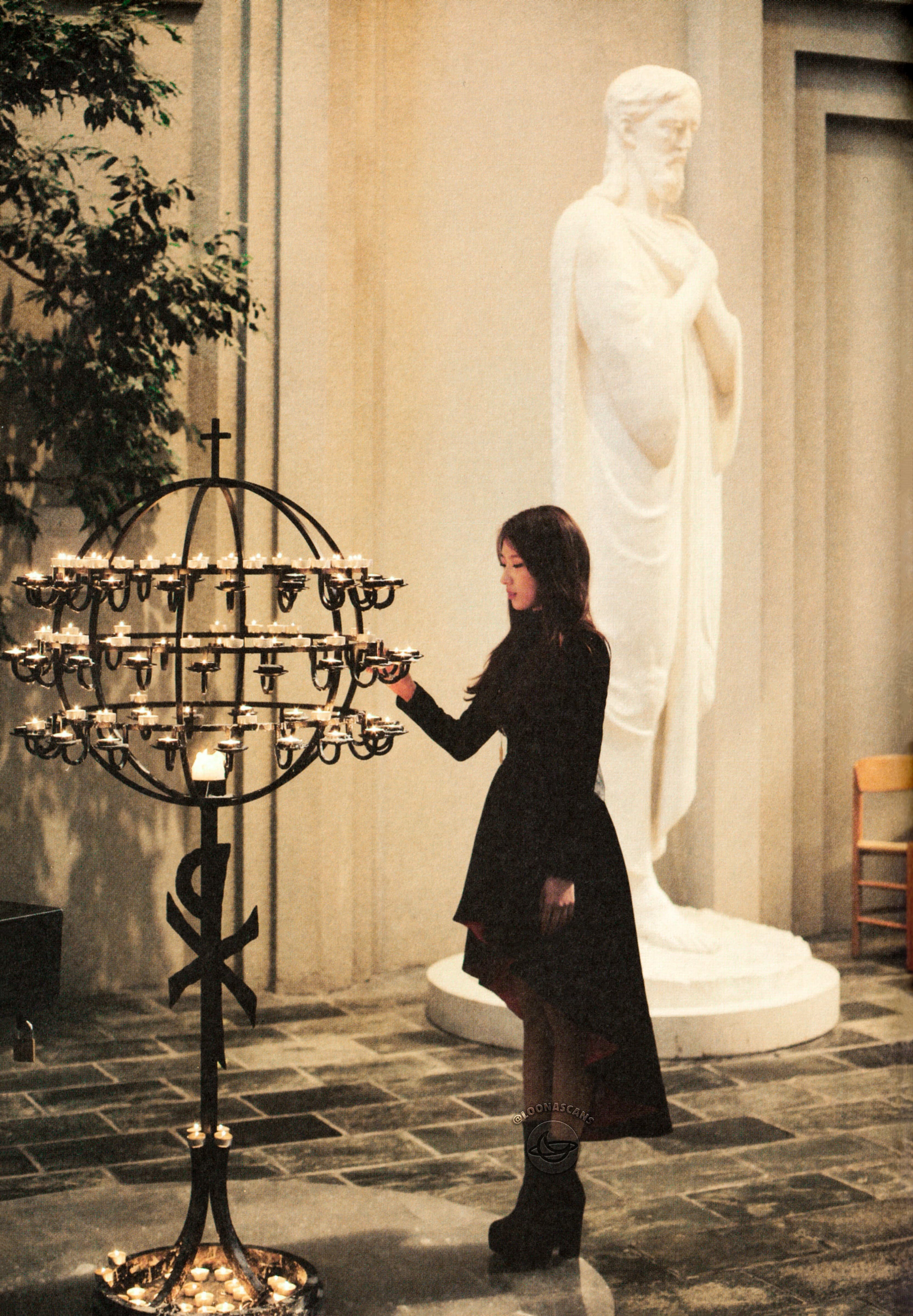 Haseul standing in front of a candle display. There is a statue of Jesus in the background.